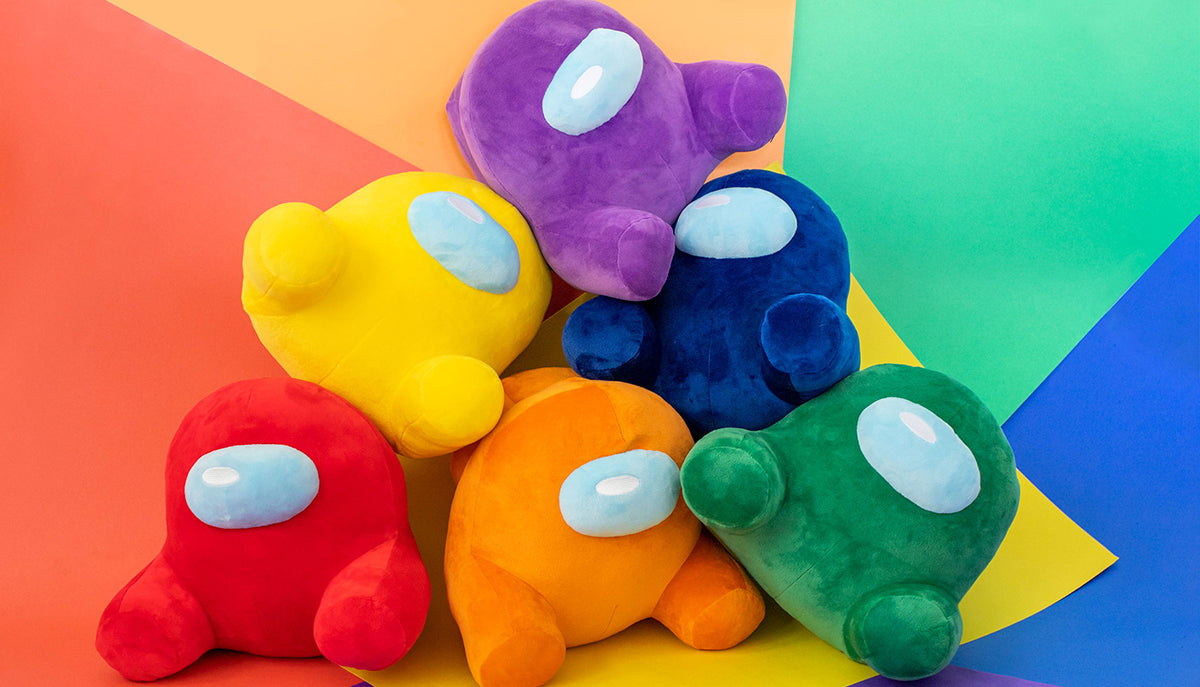 A pile of Among Us: Sitting Crewmate Plush in front of different colored squares of craft paper.