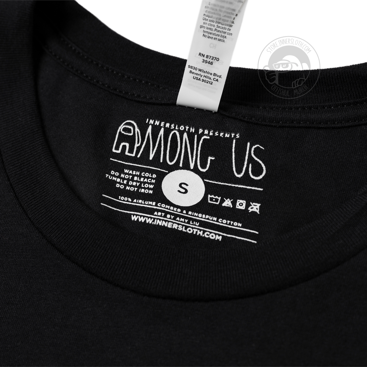 A close up photograph of the tag and printed information on the inside of the shirt. The text reads “Innersloth presents Among Us.” There are several symbols that show the following care instructions wash cold, do not bleach, tumble dry low, do not iron. The size of the shirt is Small. Additional text reads “ 100% airlume combed &amp; ringpun cotton. Art by Amy Liu. www.Innersloth.com” 