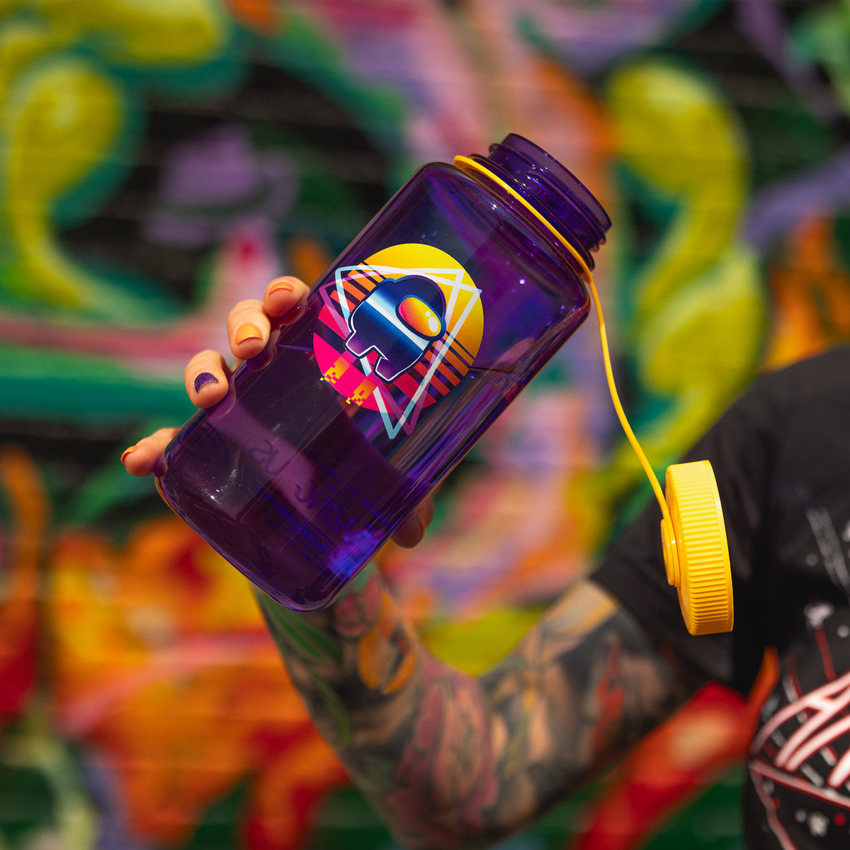 A model holding the Crewmate water bottle in front of a graffiti wall. Its yellow cap is open.