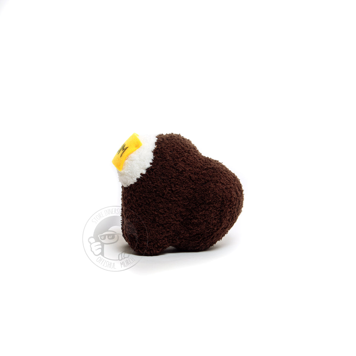 A profile view product photograph of a small, brown, fuzzy, Crewmate plush facing left with a felted DUM sticky note hanging over their visor. From this angle you can see the Crewmate’s big, round, and thick backpack. 