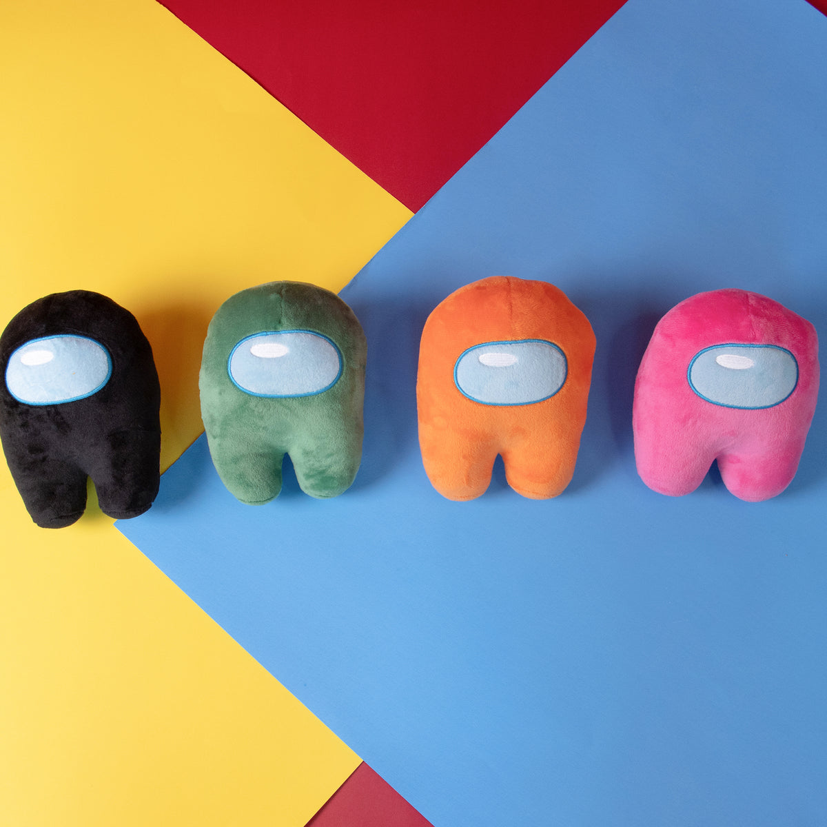 Lifestyle Photograph of a Black, Green, Orange, and Pink Crewmate Plush by Frisk Wolfie Standing in a row against a yellow, red, blue color blocked background. 