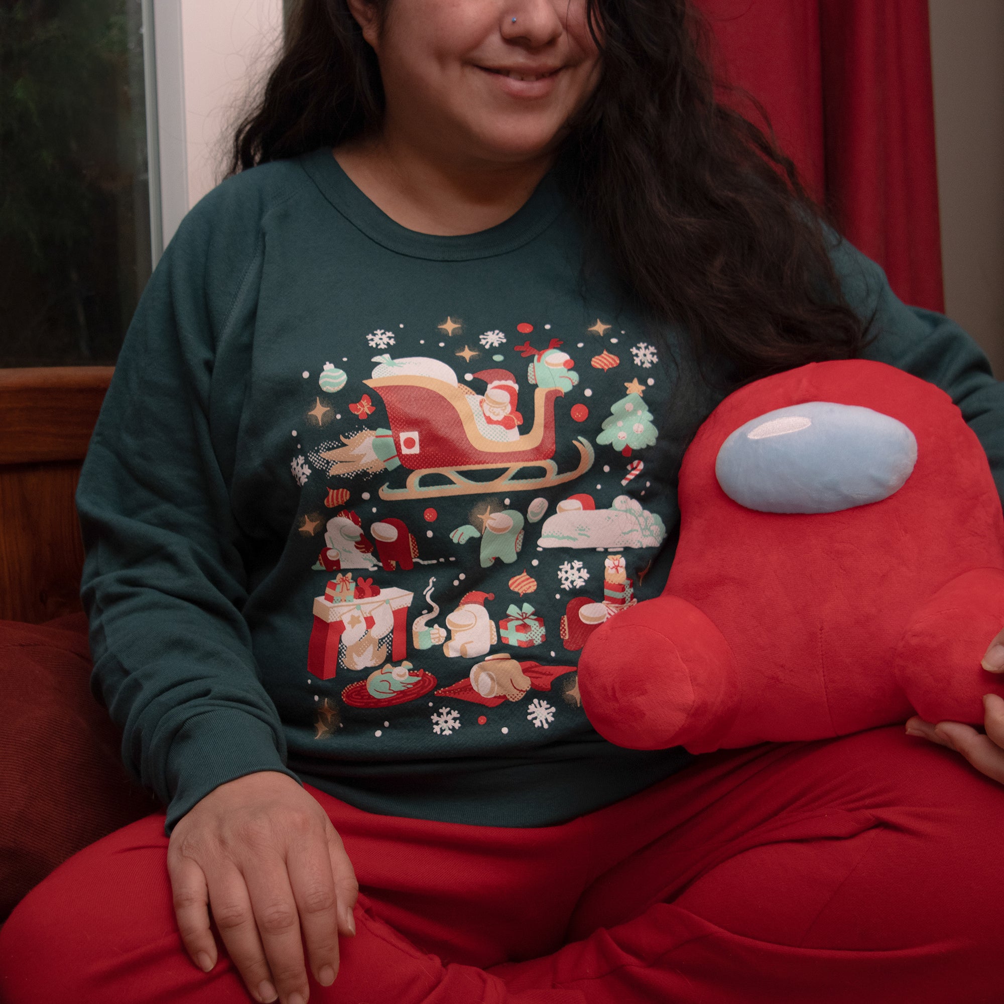 A flat lay photograph of a green longsleeve sweatshirt on a white background. The garment’s design depicts several Crewmates engaged in various holiday activities such as building a snowman, throwing snowballs, making snowforts, relaxing with cocoa, carrying presents, and taking naps. Flying overhead is a Santa and Rudolph Crewmate in a jet engine sleigh. The scene is surrounded by christmas trees, ornaments, candy canes, snow, snowflakes, bows, red noses, and starry sparkles. Designed by Mengmeng Liu