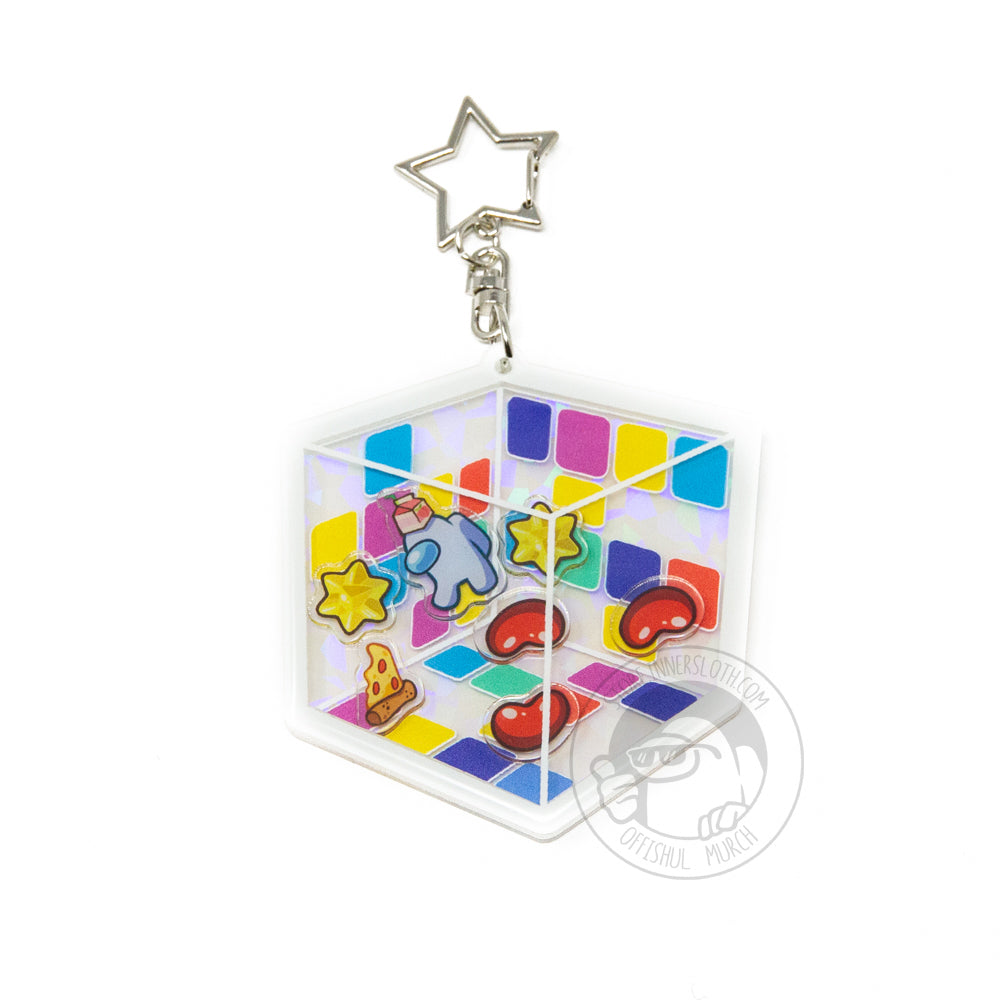 A product photo of the Among Us: Cosmicube Shaker Charm. The charm has a silver keychain in the shape of a star. It is a flat square that gives the optical illusion of a cube. The charms inside are a white crewmate with an orange juice box hat, three red beans, two yellow stars, and a slice of pepperoni pizza.
