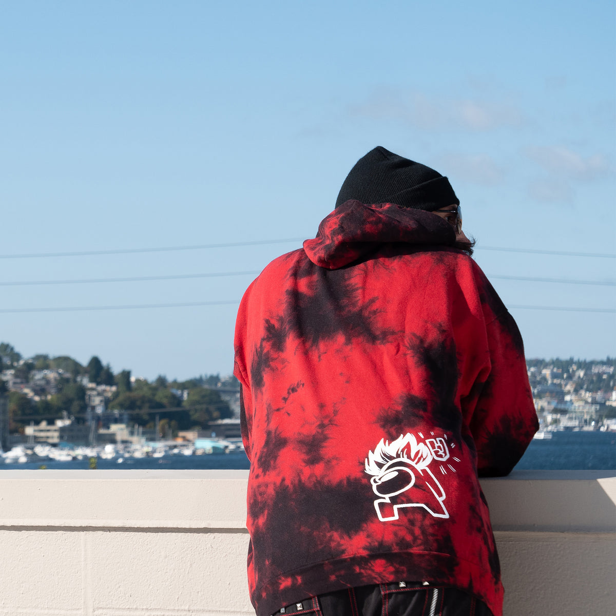 A backview of a model hunched over a railing wearing the Metal Red Pullover Hoodie. The back shows off the the Punk Crewmate screenprint detail.
