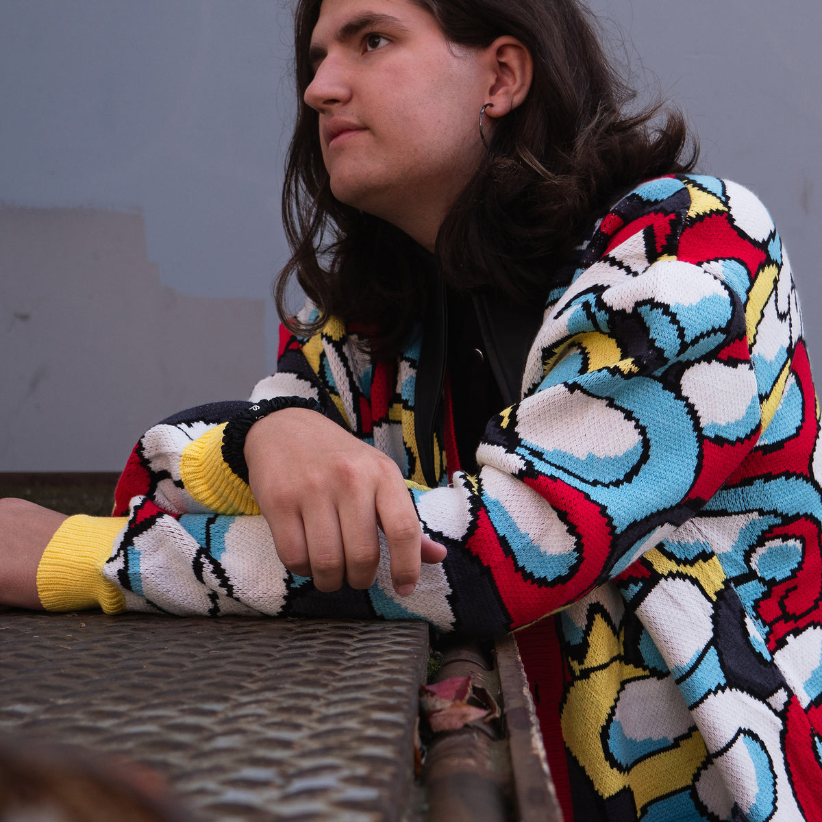 A side-view angle of a model wearing the knit cardigan, sitting at a table with their arms crossed, looking straight ahead. 