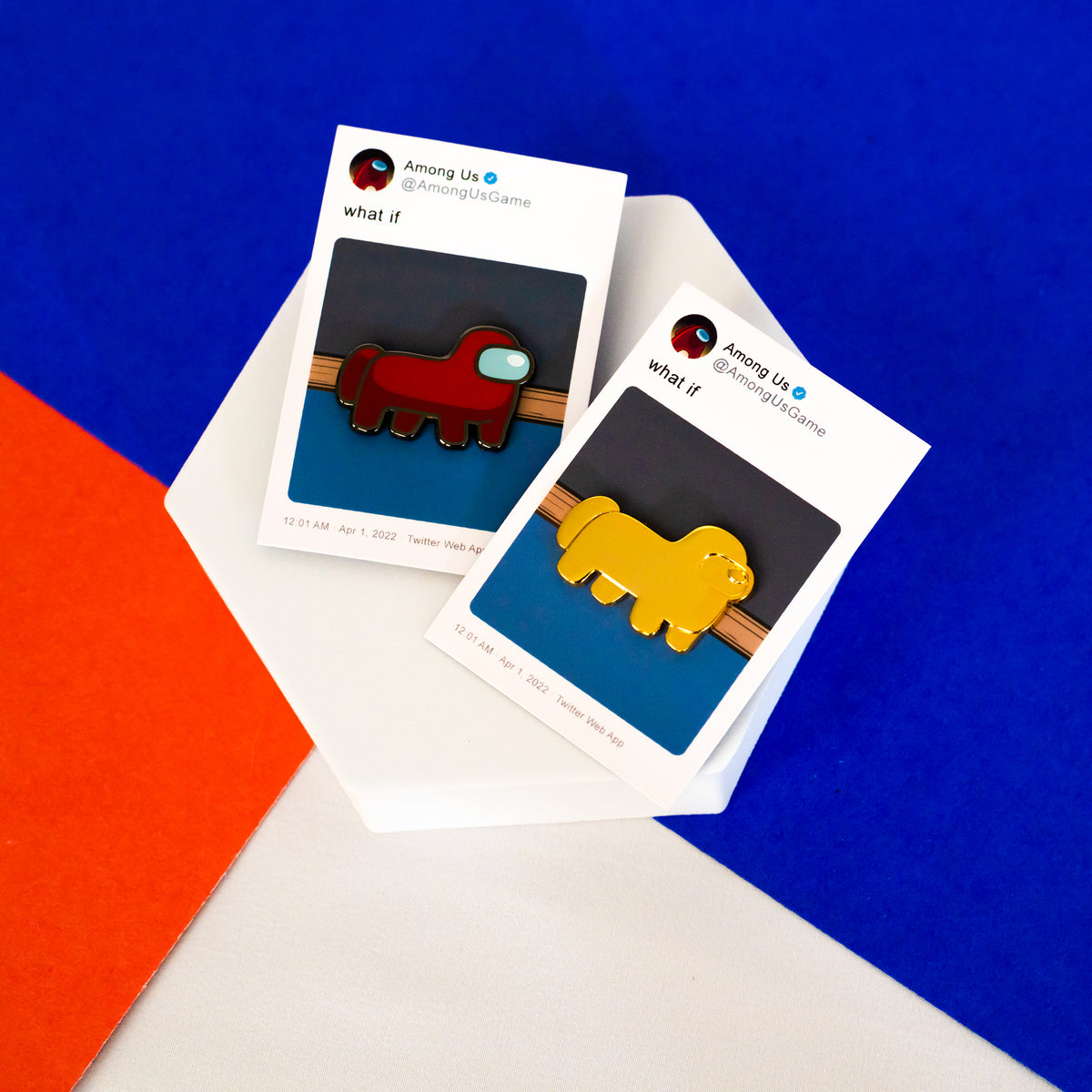 A red horsemate enamel pin and golden horsemate enamel pin on their respective backing cards are laying side by side on a colorful blue, red, and white surface.