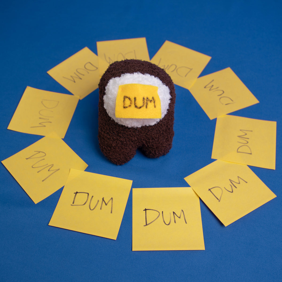 An overhead photograph of the DUM brown Crewmate surrounded in a circle of yellow sticky notes that all say DUM.