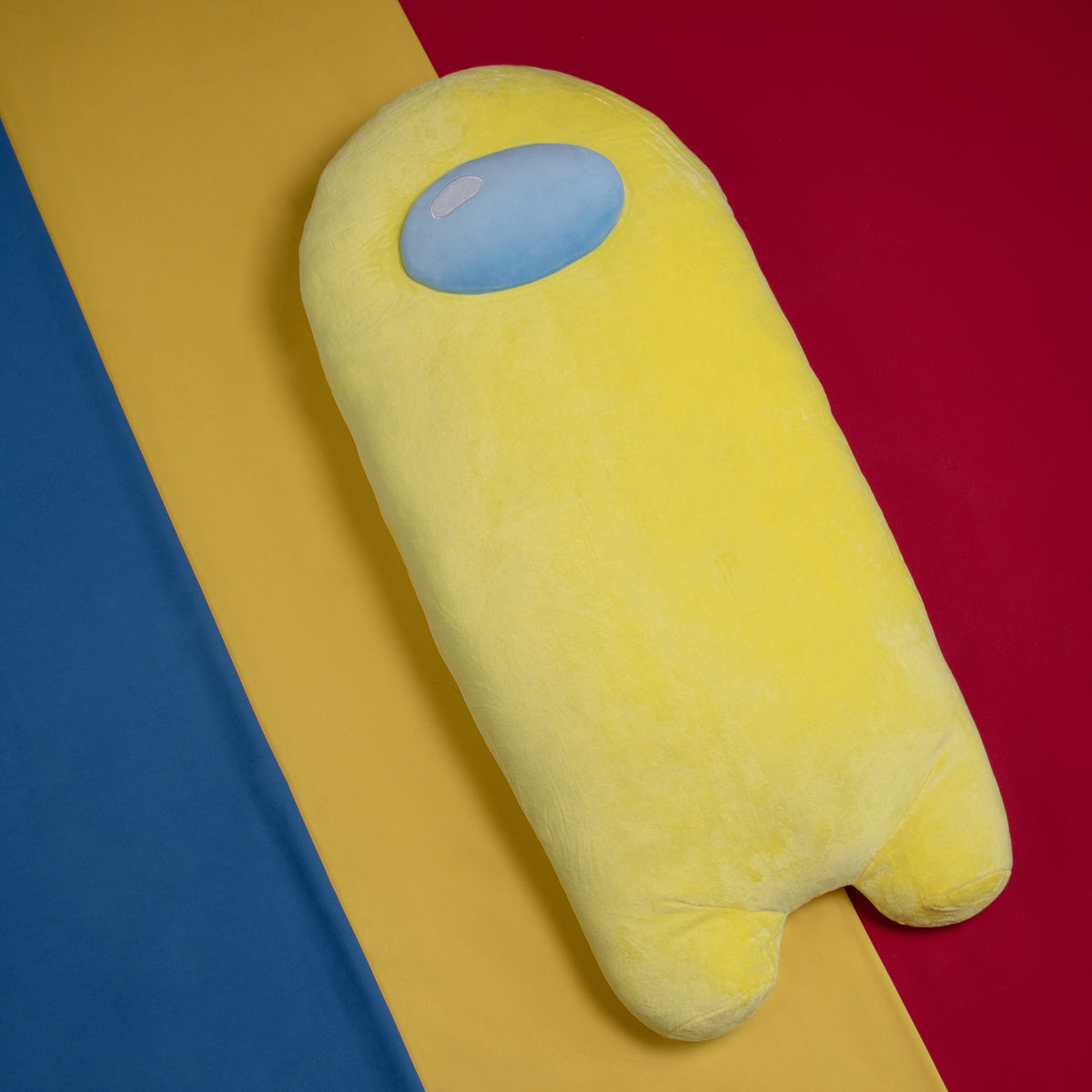 A lifestyle photograph of the yellow longbean plush laying against a blue, yellow, and red background. 