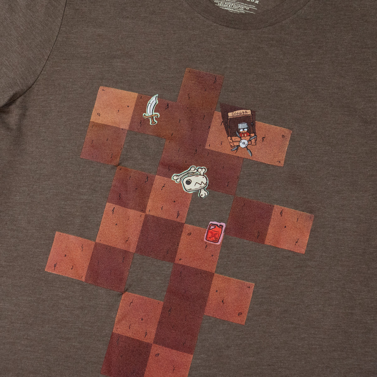 A close-up of a brown T-shirt with a brown square pattern on it, skewed slightly to the right and cropped closely to show the shirt design. Scattered on the brown square pattern are a cuirass, an animal skull, a wooden stall saying “Digger” with a person behind it, and a jar of gasoline. The brown T-shirt is on a white background.