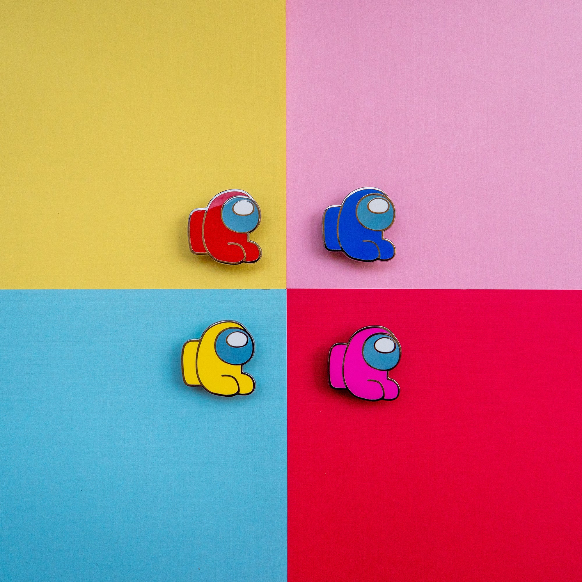 A product photograph of all four color variants of the Among Us: Mini Crewmate Enamel Pin. The Mini Crewmate pins are in a sitting position and are available in red, blue, yellow, and pink.