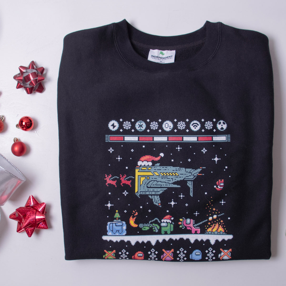 A photograph of the black Northern Hemisphere longsleeve sweatshirt folded and arranged onto a scene next to a tiny ornaments, ribbon, and bows. 