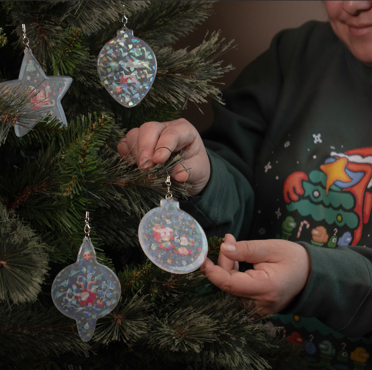 A photograph of a model hanging the Crewmates Acrylic Ornament Set on a christmas tree. 