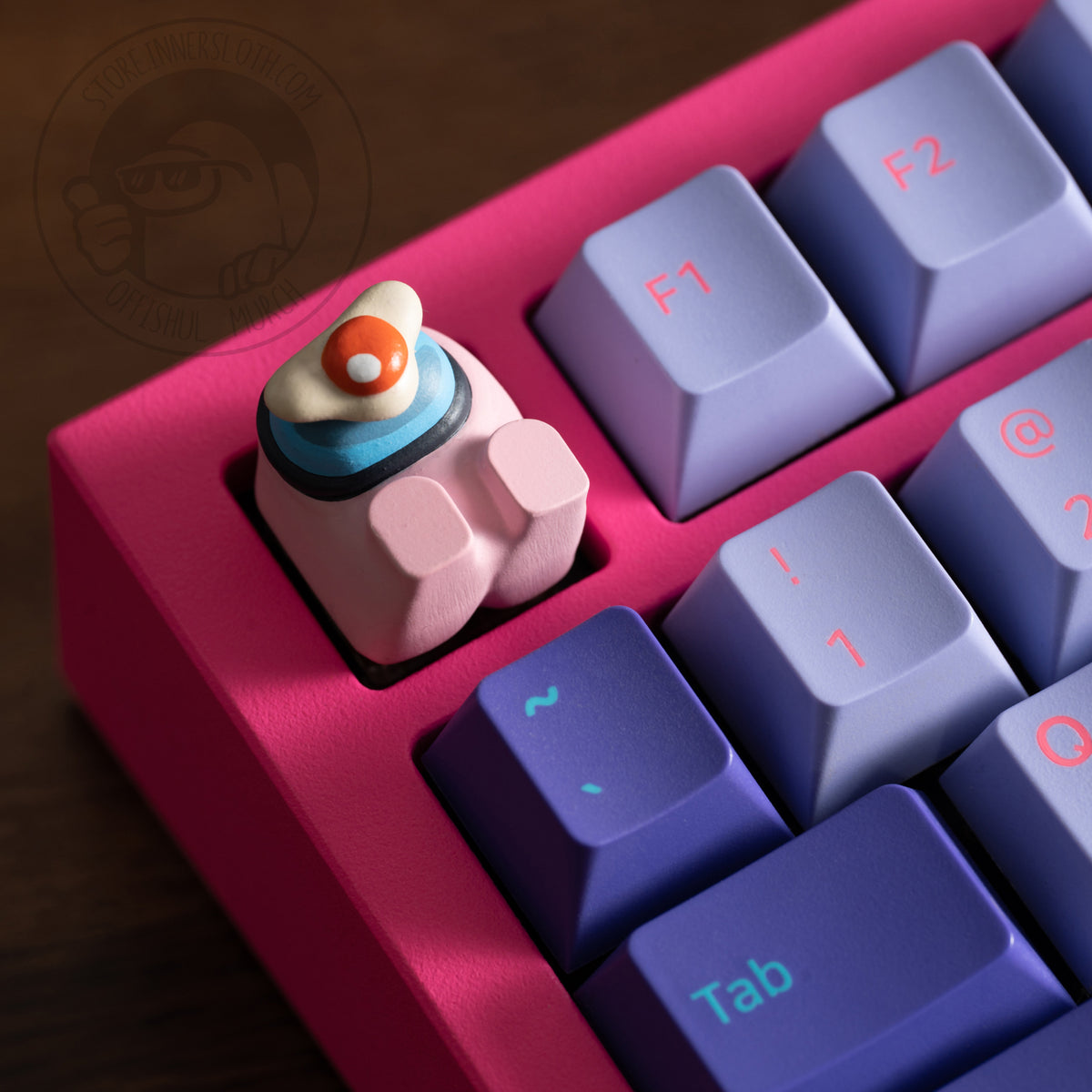 A lifestyle photo of the rose crewmate keycap taking the place of the escape key on a pink keyboard. The keycap figure lays on its back, and is shown with a fried egg over its visor.