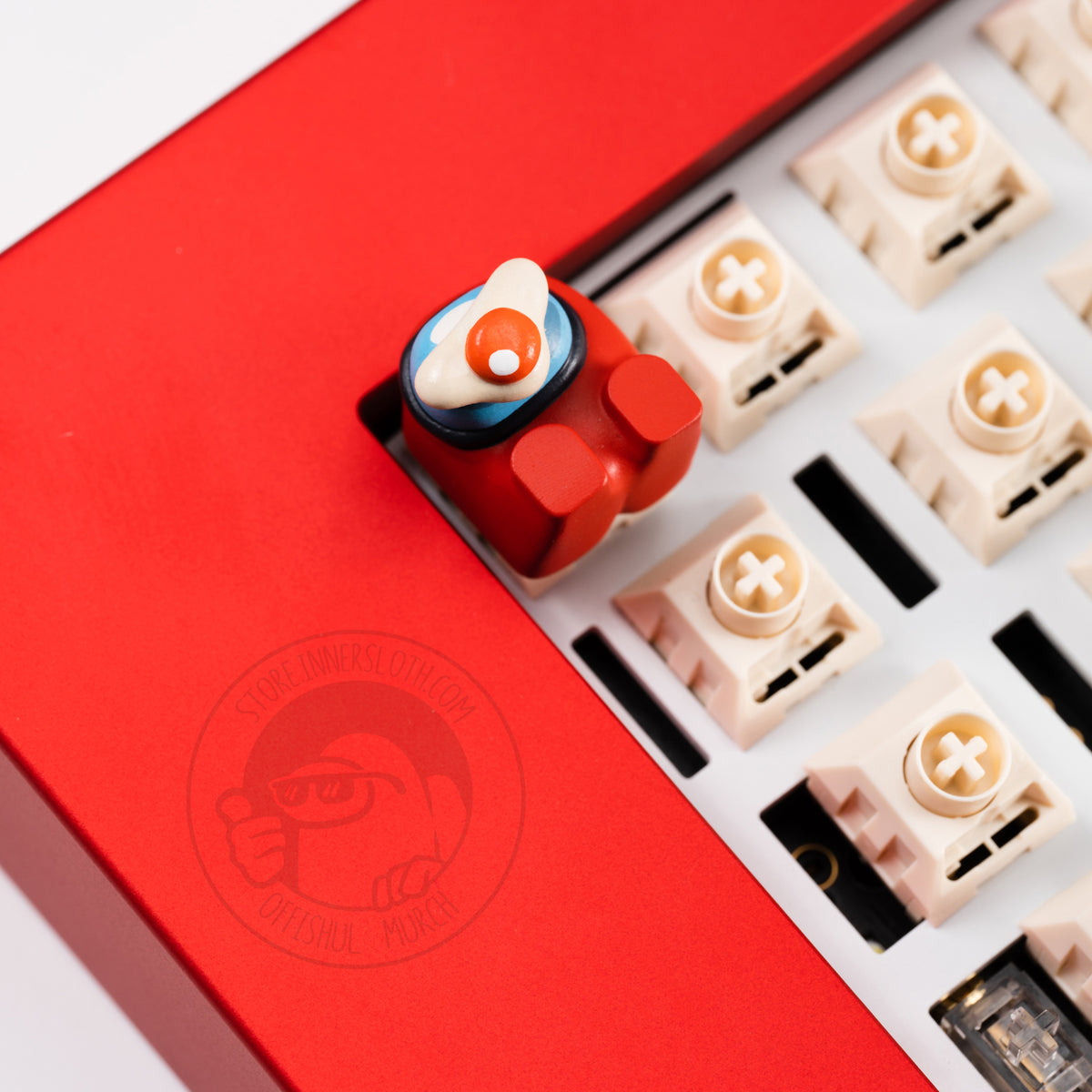 A lifestyle photo of the red crewmate keycap taking the place of the escape key on a red keyboard with missing keys. The crewmate keycap figure lays on its back, and is shown with a fried egg accessory over its visor.
