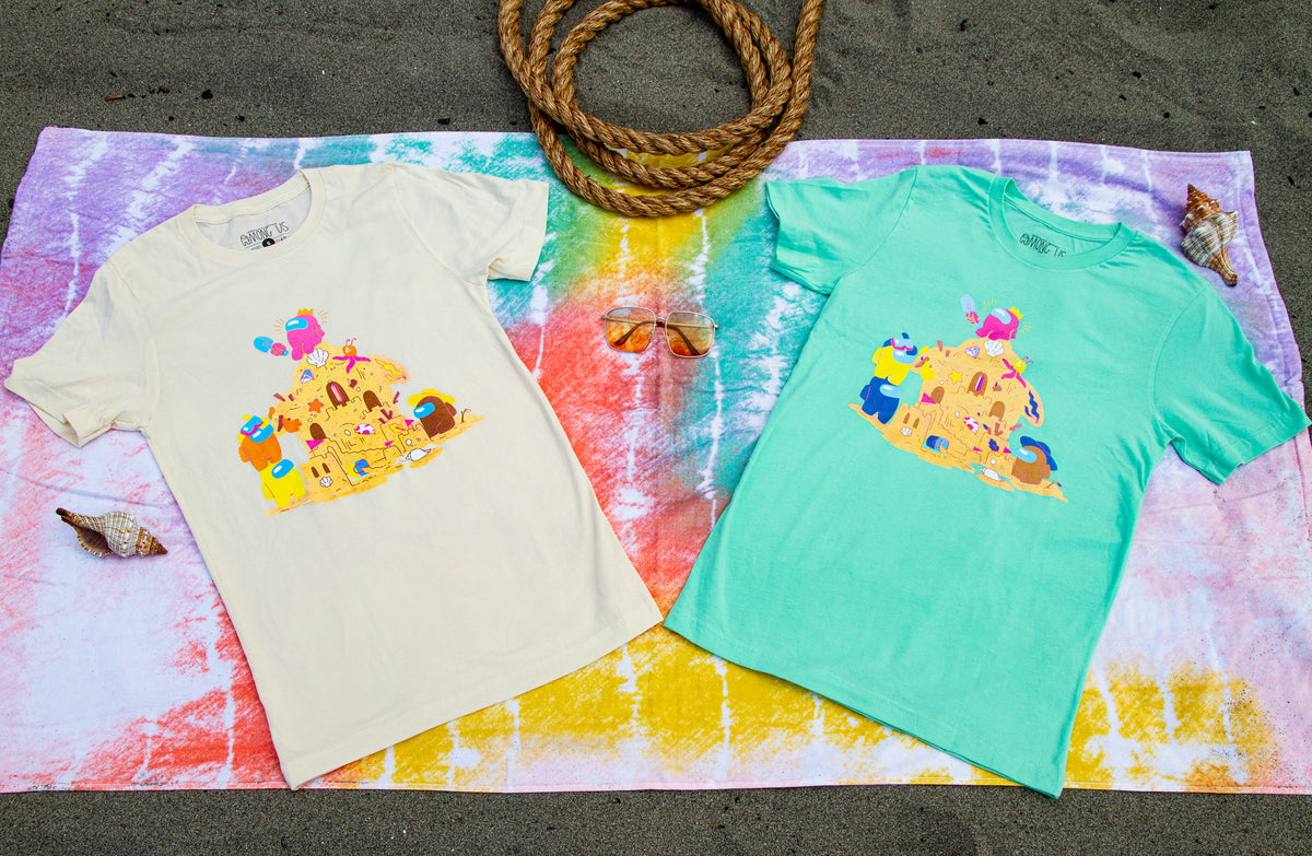 The Among Us: Sandcastle Tee in Mint lays beside the Among Us: Sandcastle Tee in Natural on a tye dye towel.