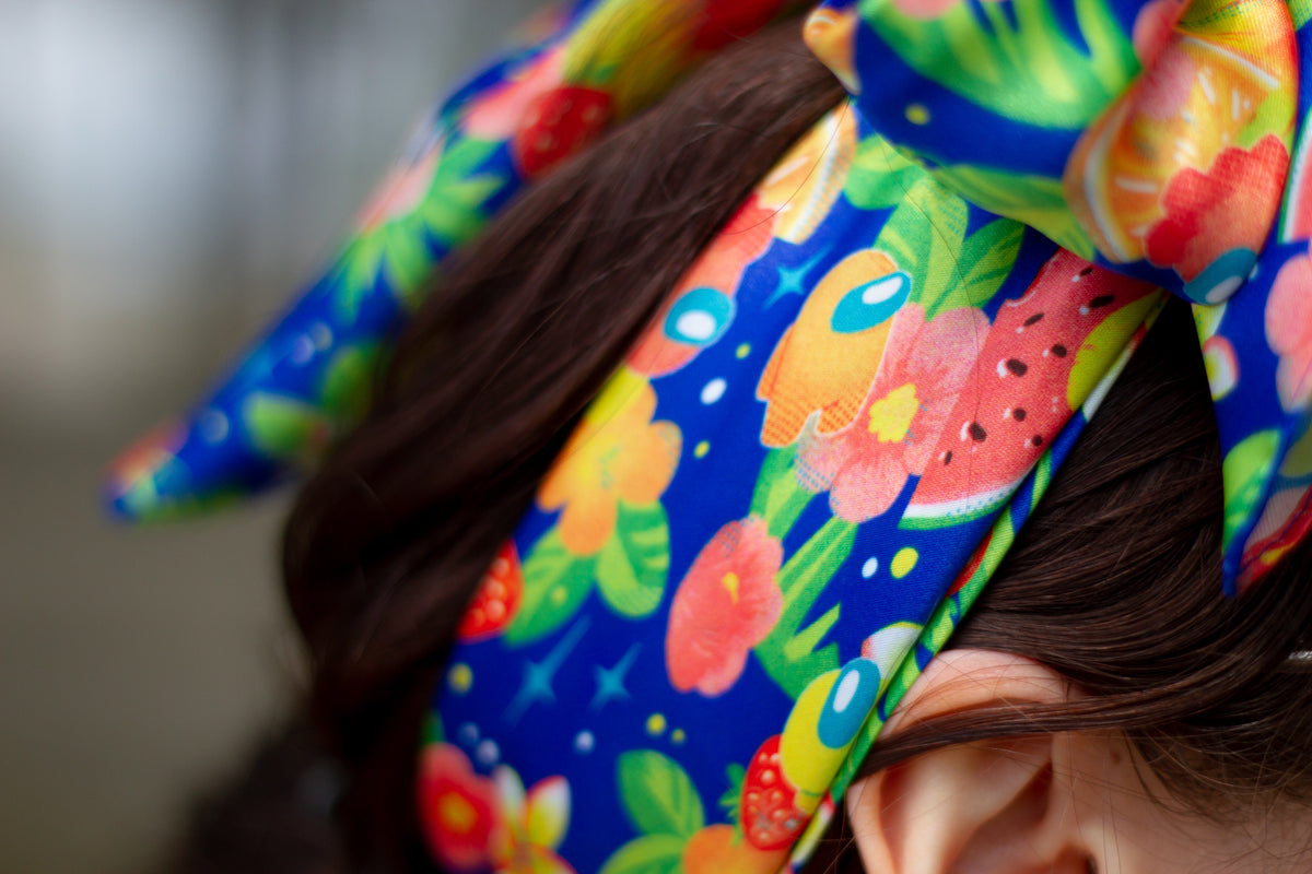 A closeup of a the Among Us: Tropical Crewmate Scarf in blue on a model, folded into a tied bow.