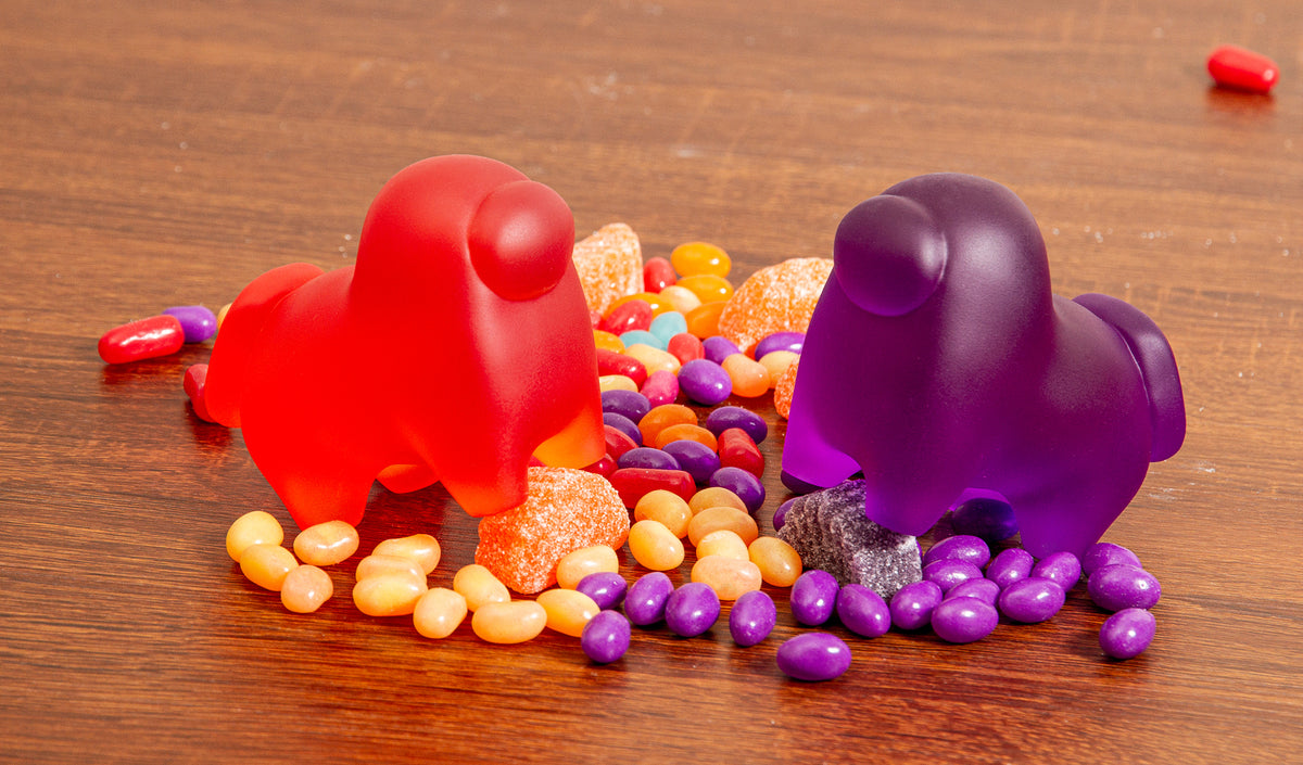 Two Horse-shaped Crewmate figurines, one orange, and one purple, standing on a colorful bed of jellybeans and assorted sugary-sweet candies