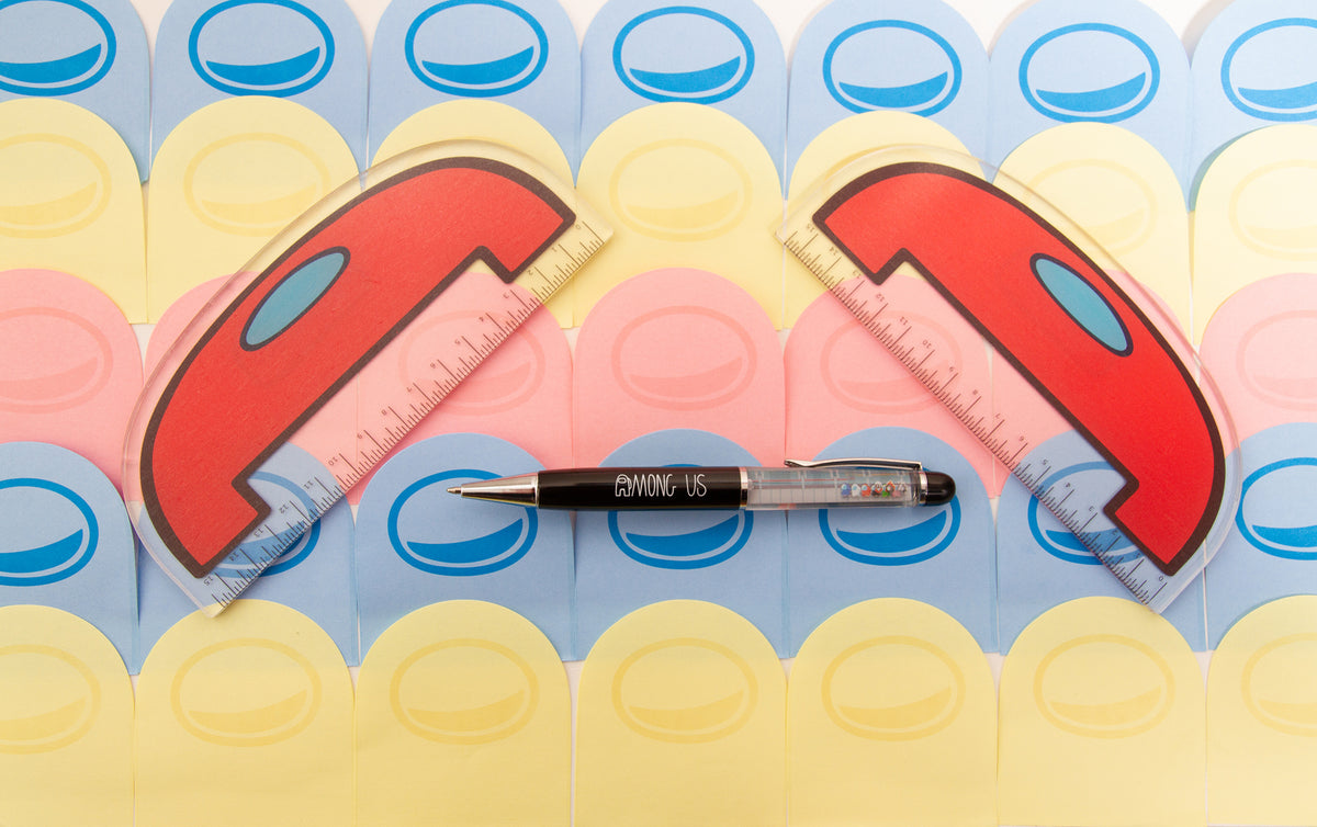 The Among Us Crewmate Floaty Pen by Noble Demons sitting on a lined-layered, alternating color (yellow, blue, pink), Crewmate shaped sticky note background. The pen is framed by two Red wide Crewmate Acrylic Ruler on either side of it.